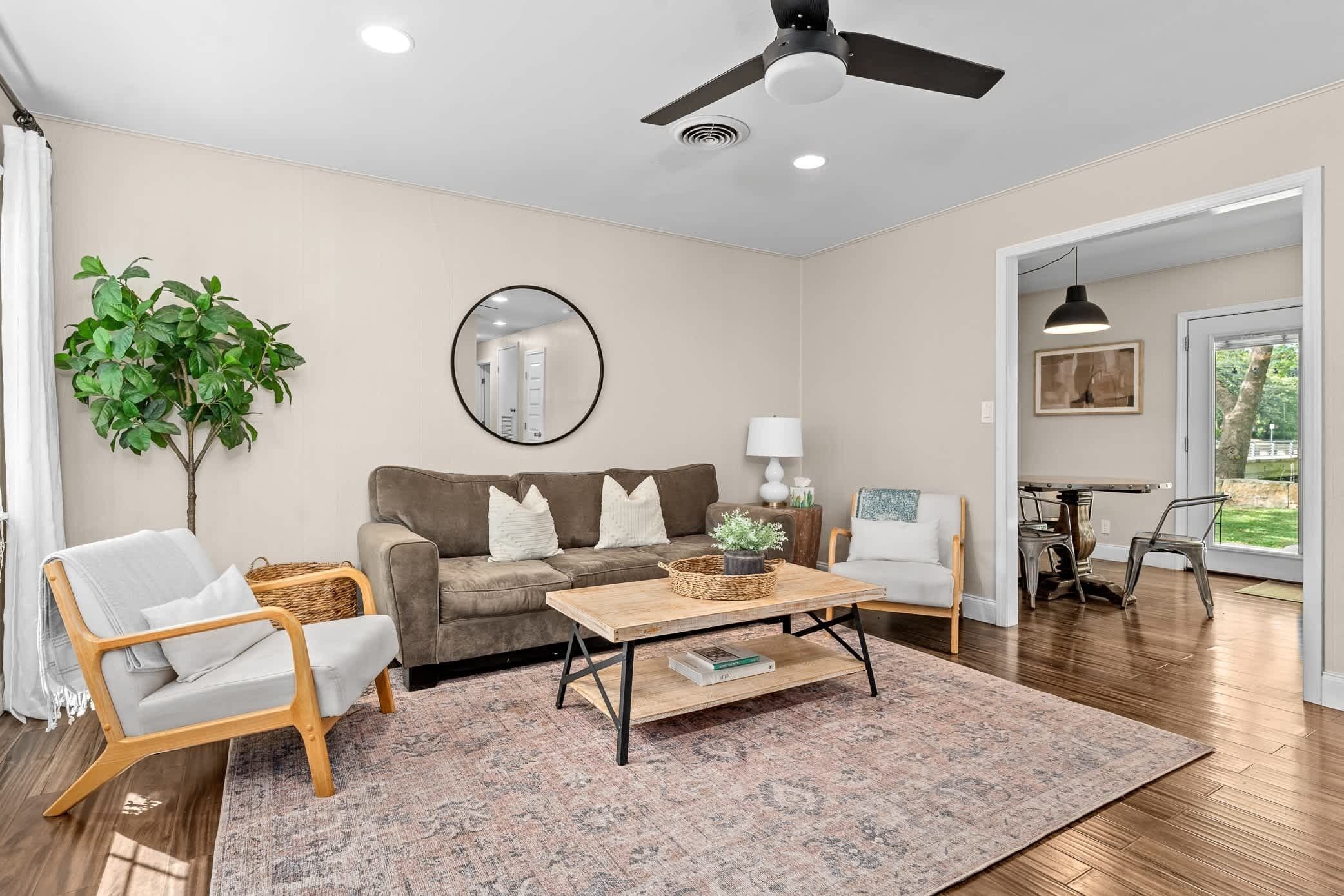 A living room with a sofa, two armchairs, a coffee table, a floor lamp, a mirror, and a ceiling fan.