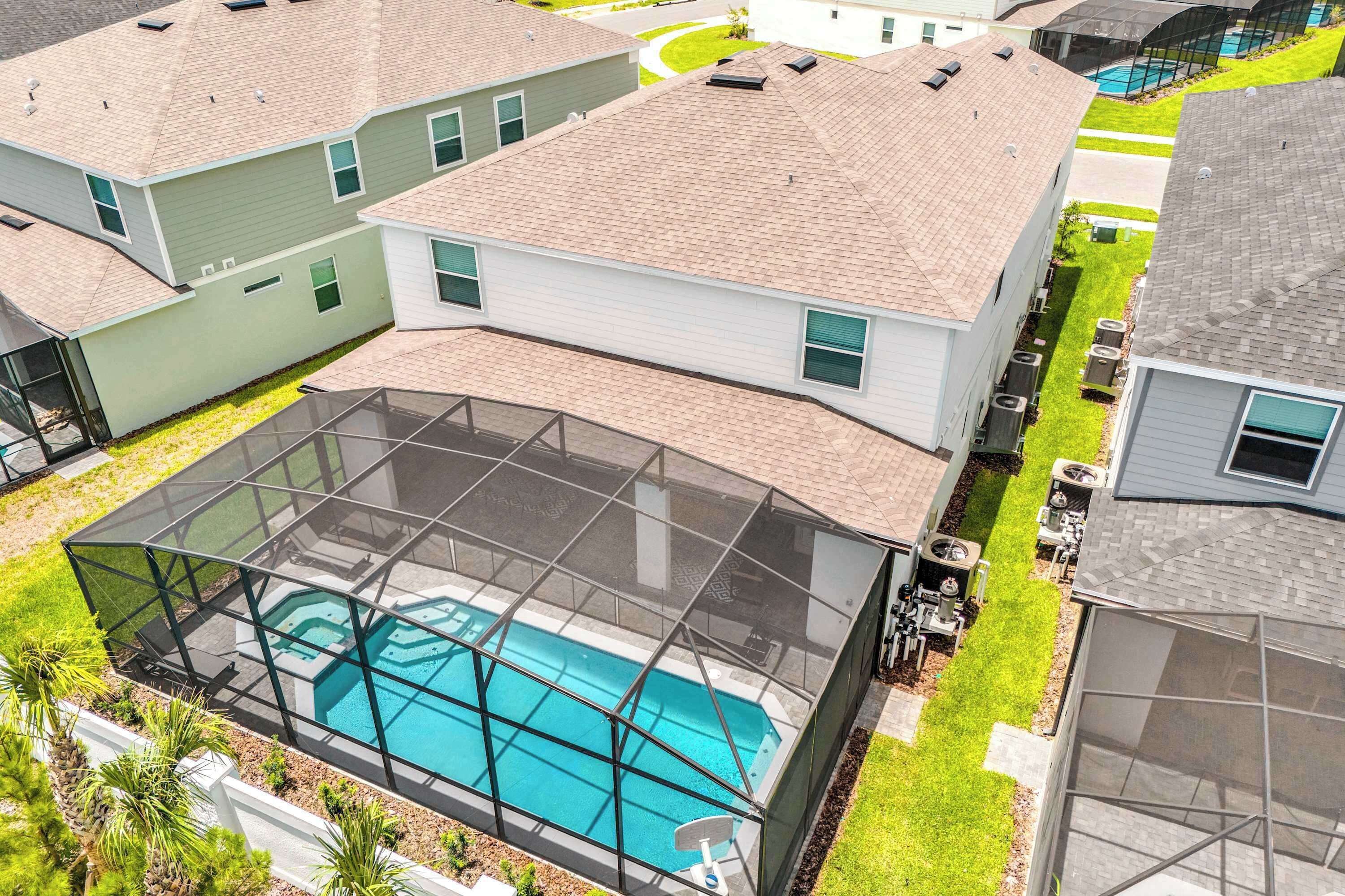 A residential area with a swimming pool covered by a glass enclosure, surrounded by well-maintained lawns and neighboring houses.