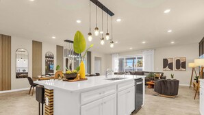 Una cocina moderna con una isla central, iluminación colgante y vistas al área de estar.