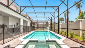 Una piscina con zona cubierta, rodeada por un patio de ladrillo y una valla metálica.