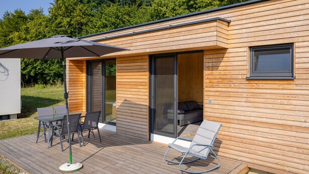 Una cabaña moderna de madera con terraza, una mesa y sillas, y una silla de descanso.