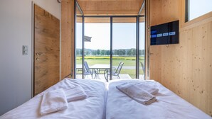 Habitación con dos camas, un televisor montado en la pared y vistas a un campo verde a través de puertas de vidrio amplias.