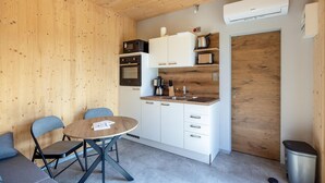 Cocina compacta con armarios blancos, microondas, cafetera y lavabo. Hay una mesa redonda con dos sillas y un bote de basura.