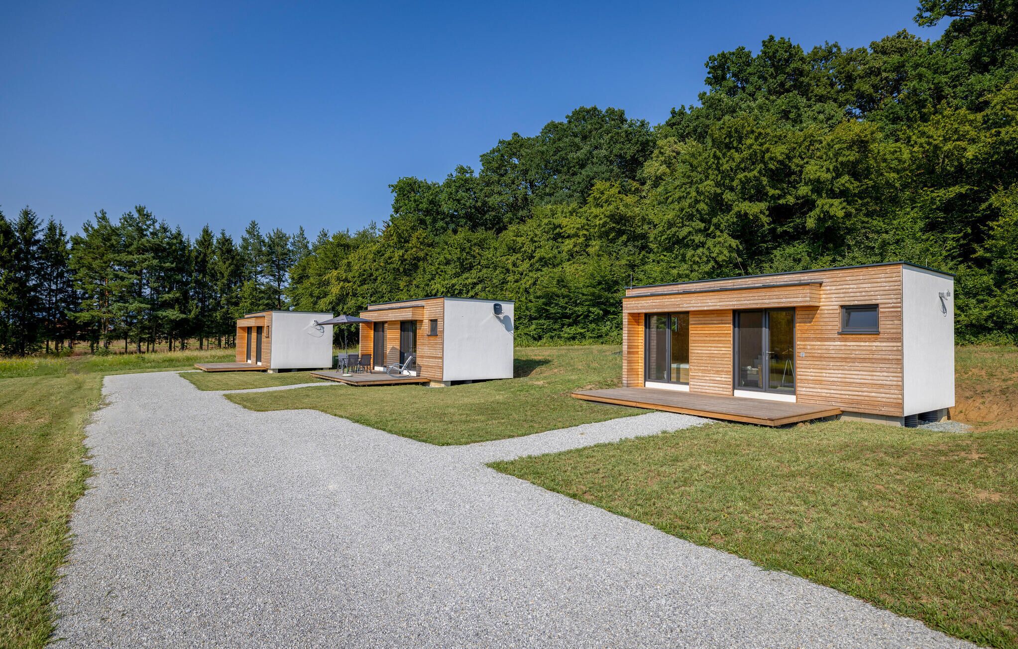 A modern outdoor cabin with a gravel path leading to it, surrounded by a forest.