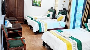 Une chambre d’hôtel avec trois lits, une armoire en bois, un bureau avec des chaises et une vue sur la ville par la fenêtre.