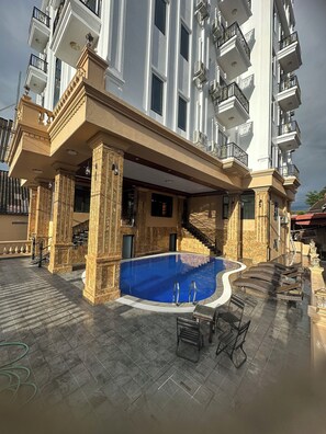 Un edifici luxós amb una piscina, seients a l'aire lliure i nombrosos balcons.