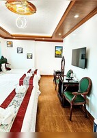 A hotel room with a large bed, a desk with a chair, a television, and framed pictures on the wall.