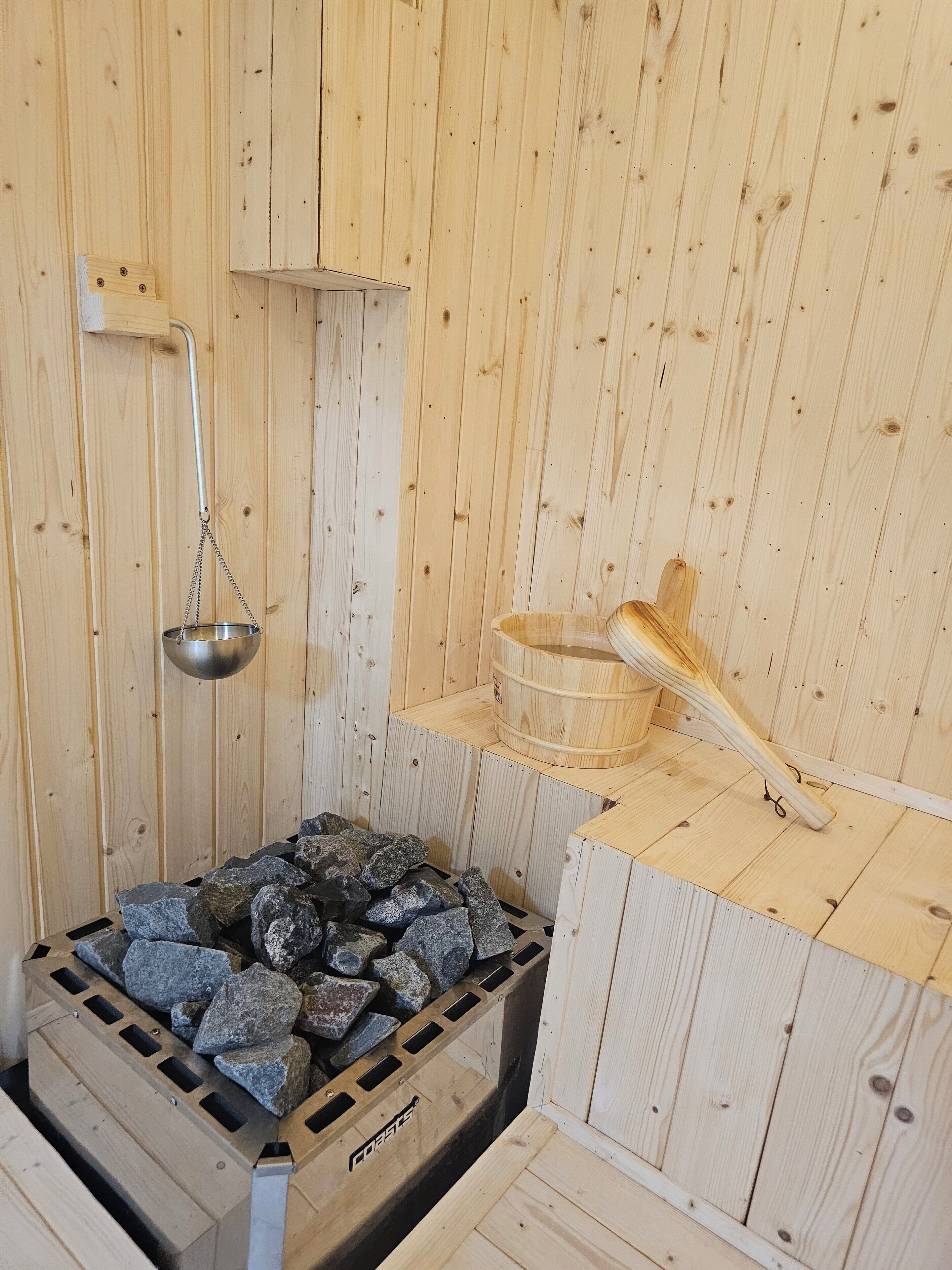 A sauna with wooden walls, a stone bench, a metal basin, and a wooden ladle.