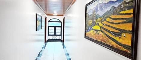 A hallway with a marble floor, wooden ceiling, and framed artwork on the walls.
