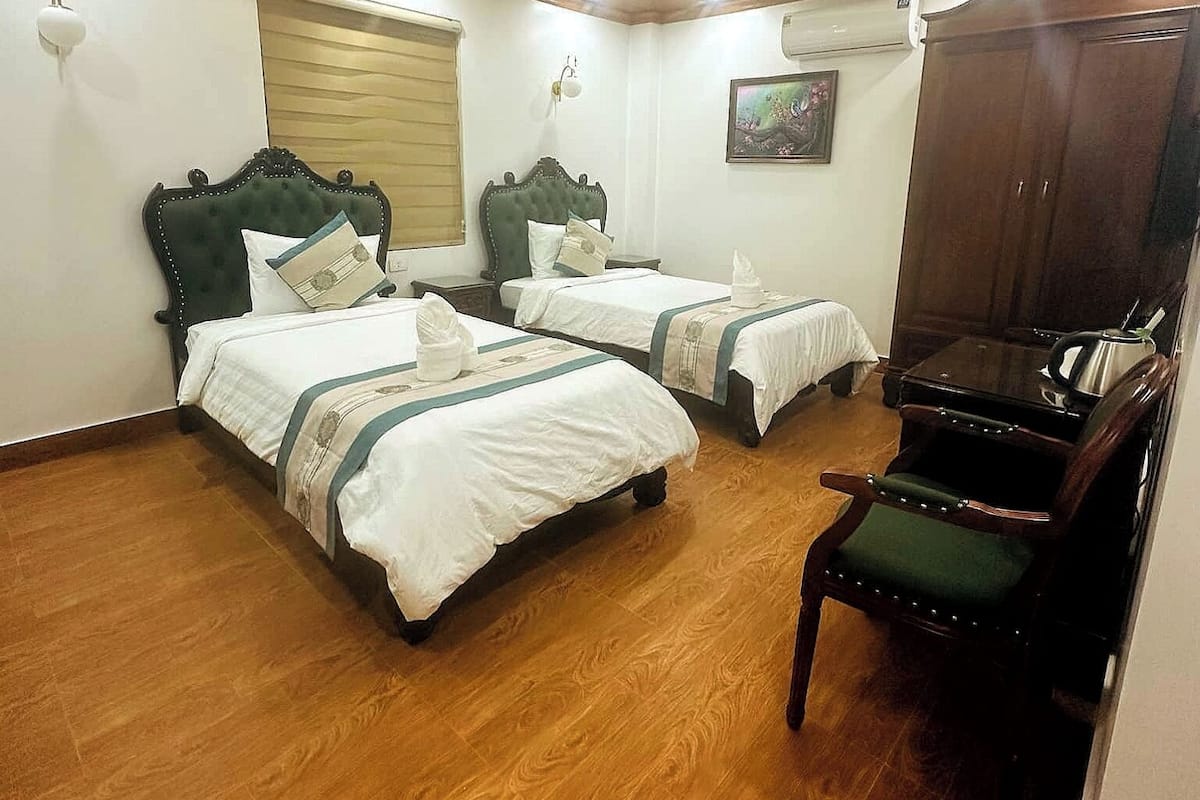 Une chambre d’hôtel avec deux lits, un plancher en bois, un ventilateur de plafond, une chaise et une armoire.