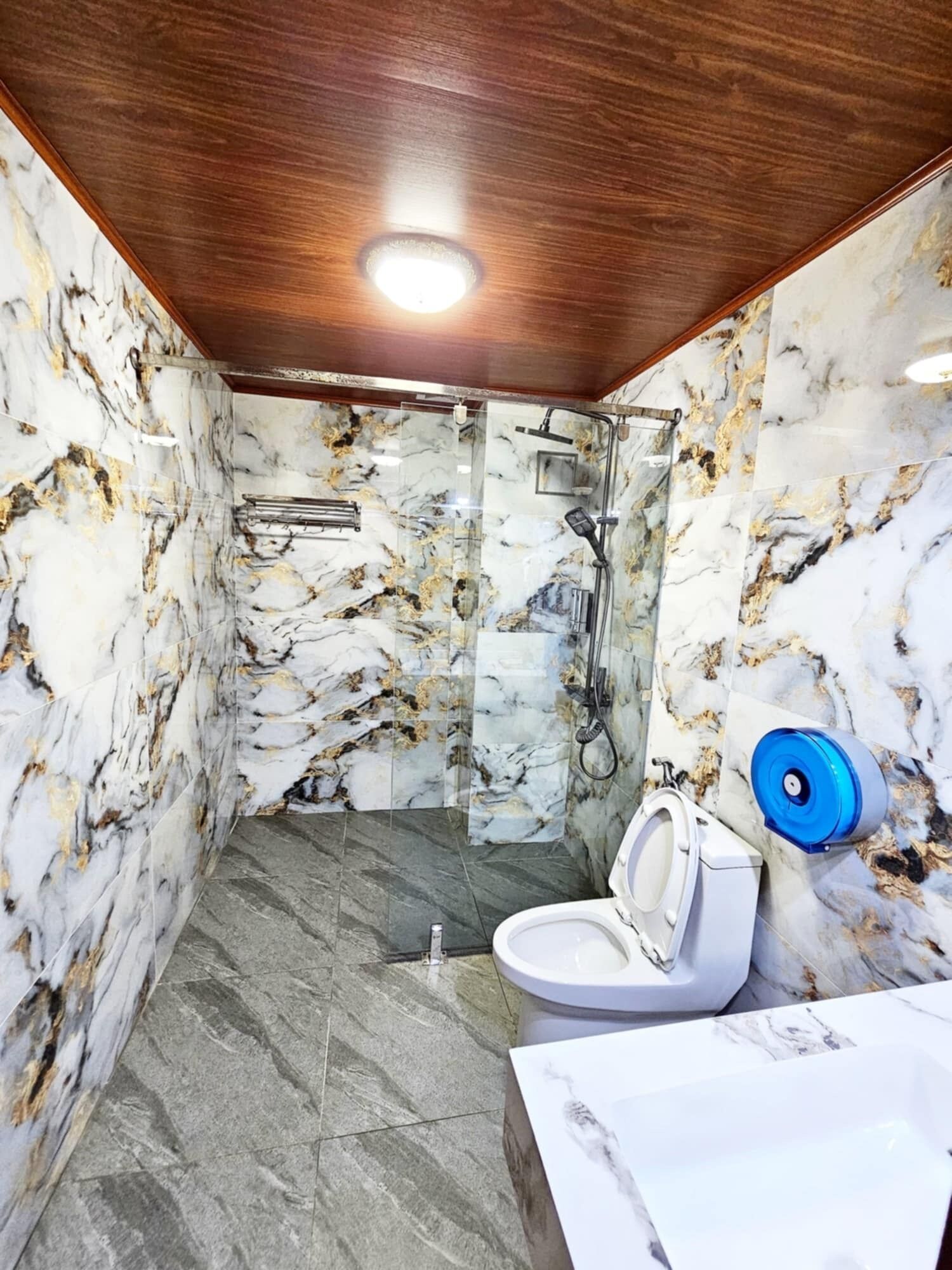 Een badkamer met marmeren wanden, een houten plafond, een douche en een toilet.
