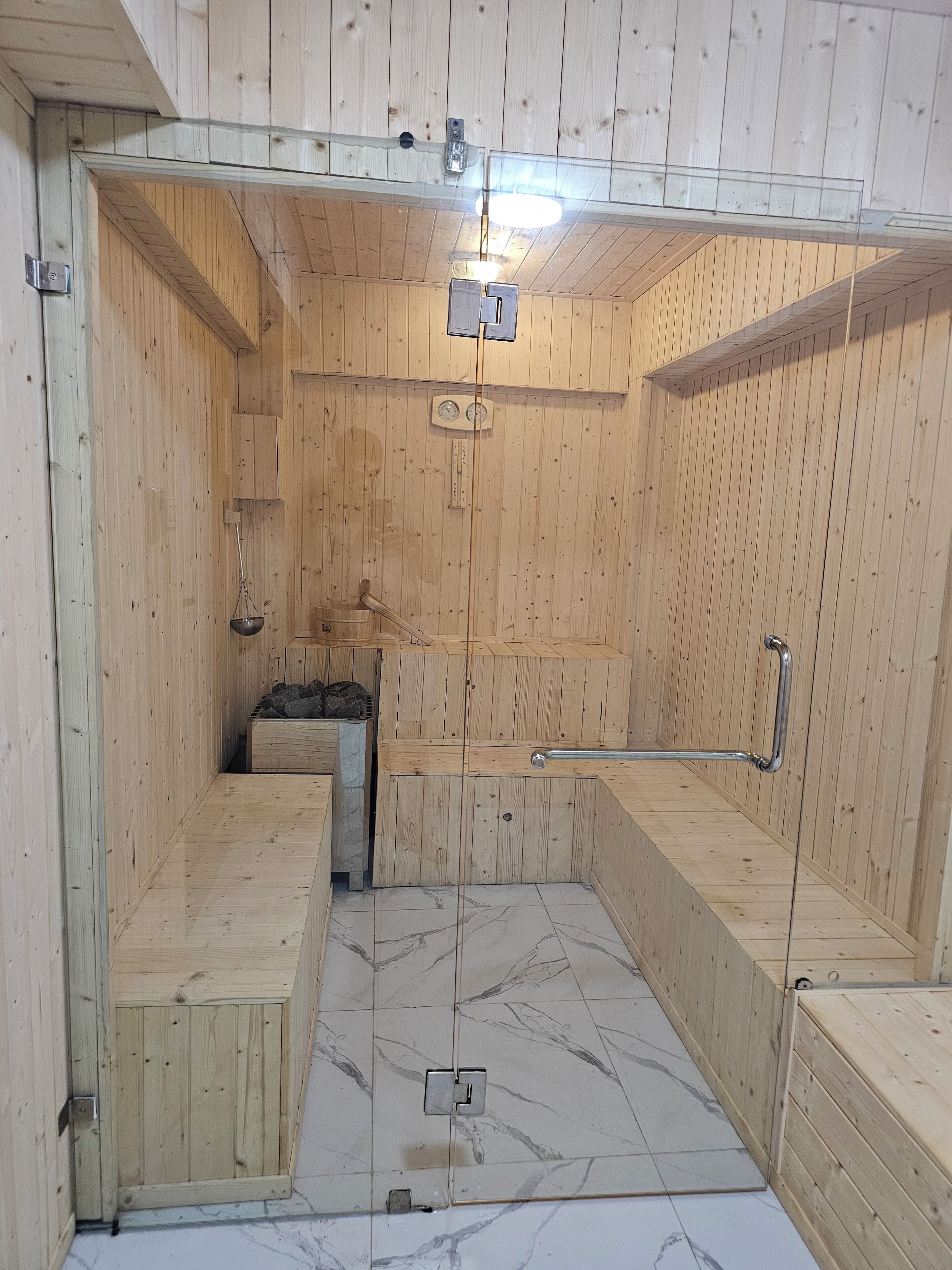 Eine Sauna mit Holzwänden und -bänken, einem sichtbaren Temperaturanzeiger und einer Metallhandstange.