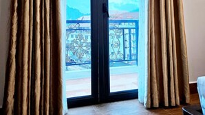 Une pièce dotée d’une porte-fenêtre coulissante donnant sur un balcon. La pièce a un plancher en bois et un meuble noir est placé sur le côté droit.