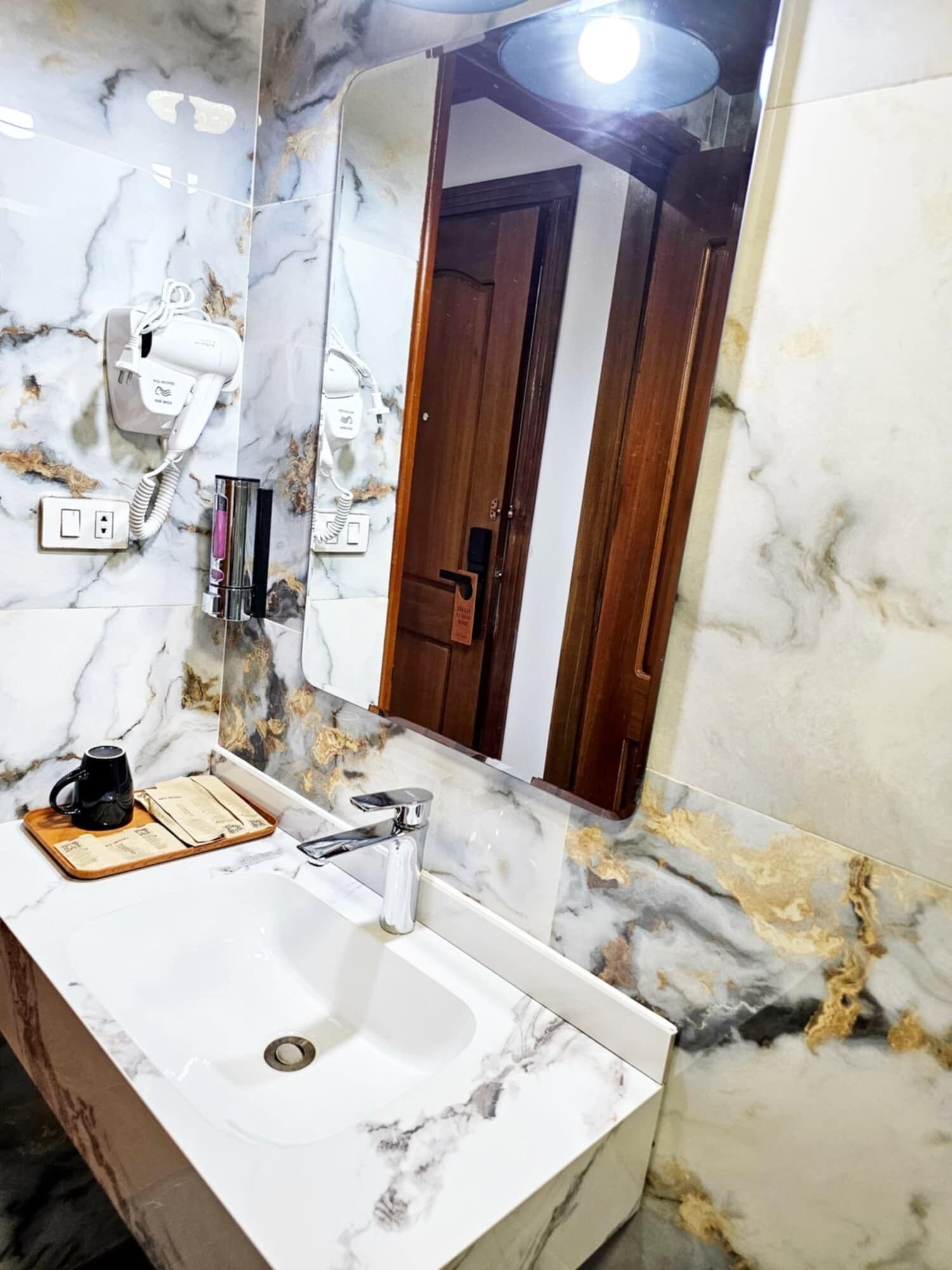A bathroom with a marble sink, a mirror, a hairdryer, and a coffee maker on the counter.