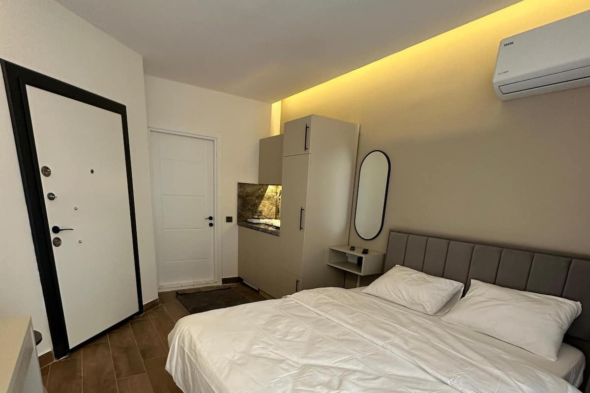 A hotel room with a large bed, a wardrobe, a bathroom with a mirror, and an air conditioning unit on the wall.