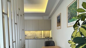 A modern kitchen with a built-in stove, a dining table with chairs, and a white partition with a decorative light fixture. - Vista Living Apartments (Trabzon)