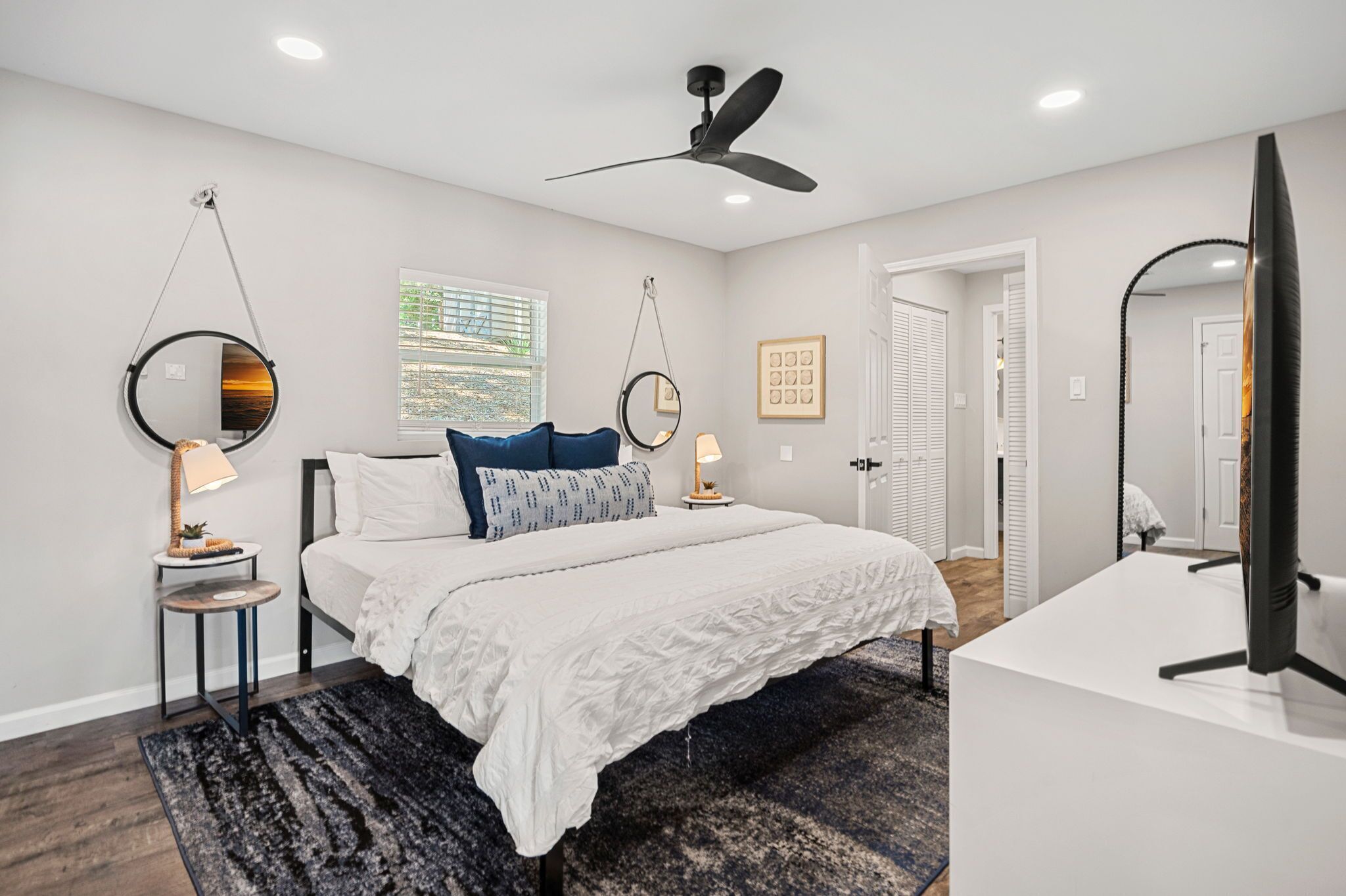 A modern bedroom with a bed, bedside tables, a ceiling fan, and a large mirror.