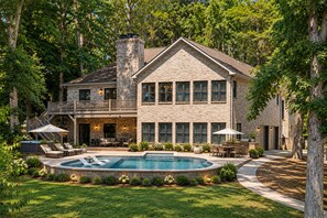 Una casa de dos pisos con piscina, mobiliario exterior y un porche cubierto.