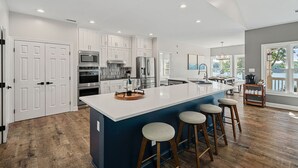 Una cocina moderna con gabinetes blancos, electrodomésticos de acero inoxidable, una isla grande con taburetes y vistas al exterior.