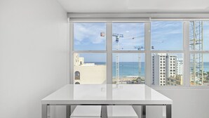 A room with a large window overlooking a beach and construction cranes, featuring a white table and a view of the ocean. - Yellow Luxury PH | Steps from the beach in Condado (San Juan)
