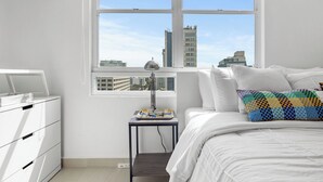 A bedroom with a bed, a nightstand, a desk, and a window with a city view. - Yellow Luxury PH | Steps from the beach in Condado (San Juan)