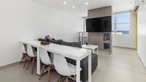 A modern living room with a white dining table, grey sofa, and a flat-screen TV mounted on the wall. - Yellow Luxury PH | Steps from the beach in Condado (San Juan)