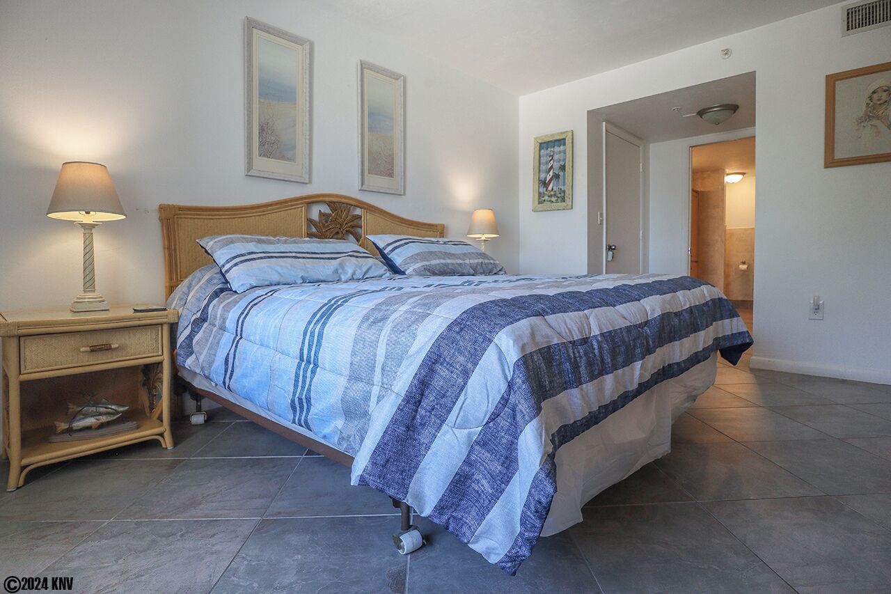 A bedroom with a bed, two bedside lamps, a nightstand, and a framed picture on the wall.