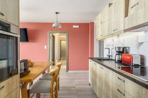 A compact kitchen with wooden cabinets, a dining table with chairs, a red toaster, and a coffee maker.