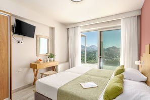 A hotel room with a bed, a desk, a mirror, a TV, and a view of the outdoors.