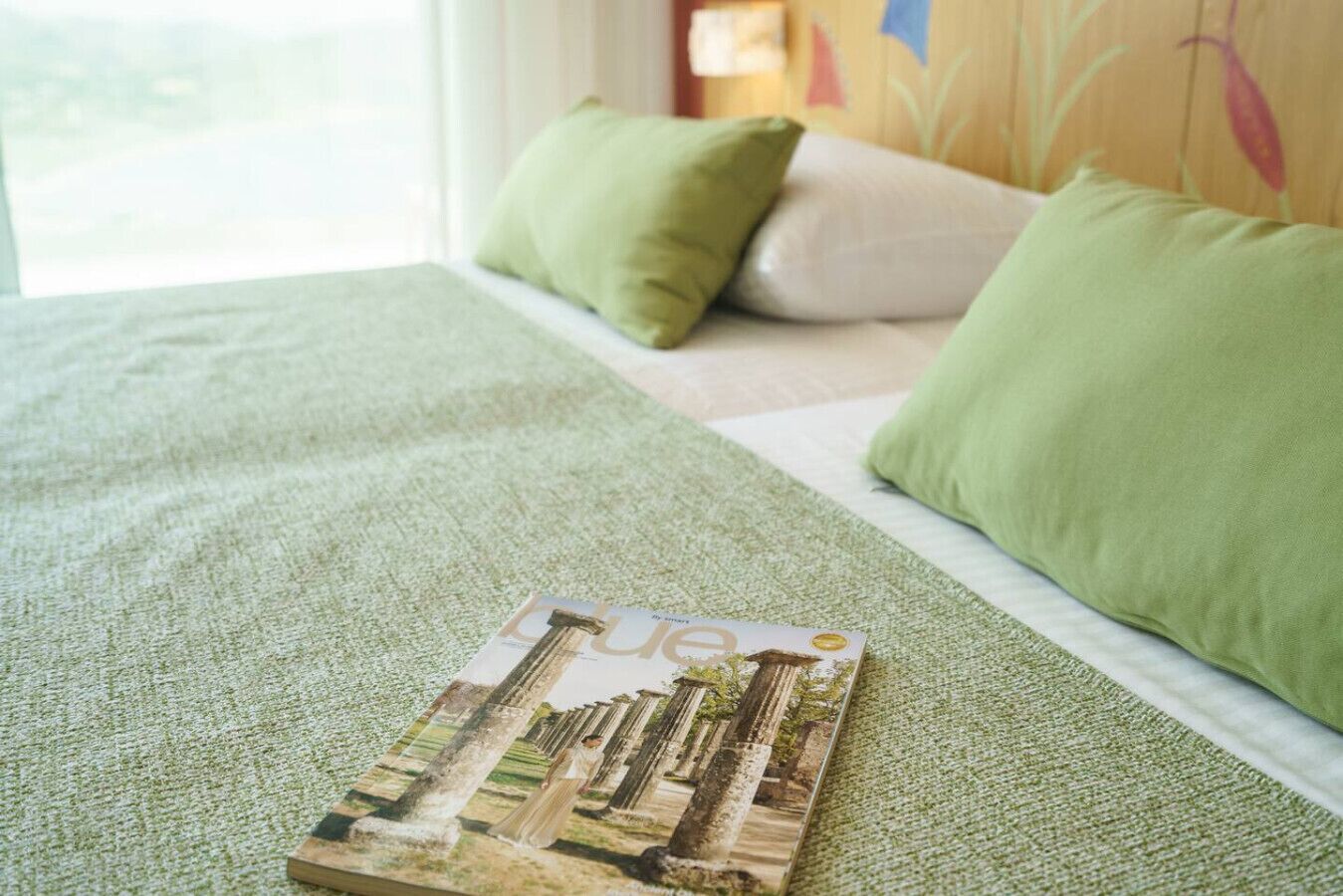 Un letto con biancheria verde, una rivista sopra e dei cuscini.
