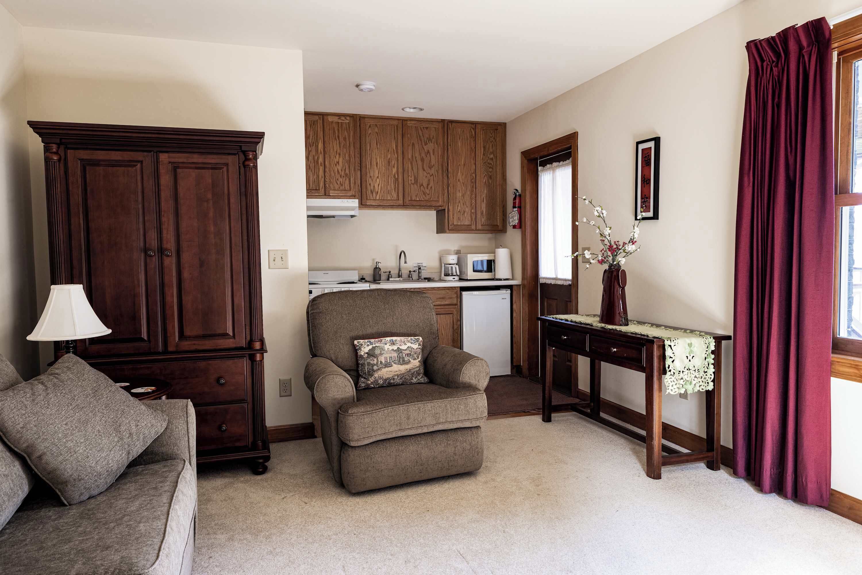 A living room with a sofa, armchair, wooden cabinet, and a small table with a vase.