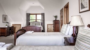 Ein Schlafzimmer mit einem großen Bett, einem Schreibtisch, einem Stuhl, einem Schminktisch und einem Fenster mit Vorhängen.