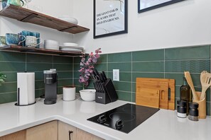 Una cocina moderna con encimera blanca, salpicadero verde y placa de cocción por inducción negra.