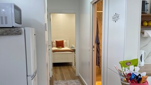 A narrow hallway with a microwave, refrigerator, and a basket of snacks on a counter.