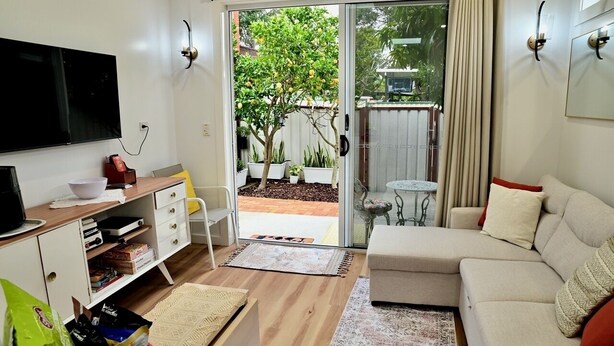 A living room with a sofa, a TV, a coffee table, and a sliding glass door leading to a garden.