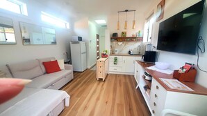 A compact living space with a sofa, kitchenette, and a TV mounted on the wall.