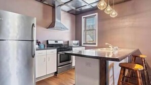 Une cuisine moderne dotée d’appareils électroménagers en acier inoxydable, d’un îlot central et de luminaires suspendus.