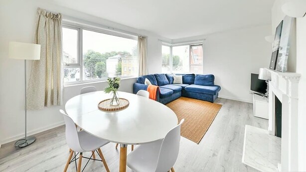 A modern living room with a white dining table, blue sofa, and a fireplace. - The Elden - No.14 (London)