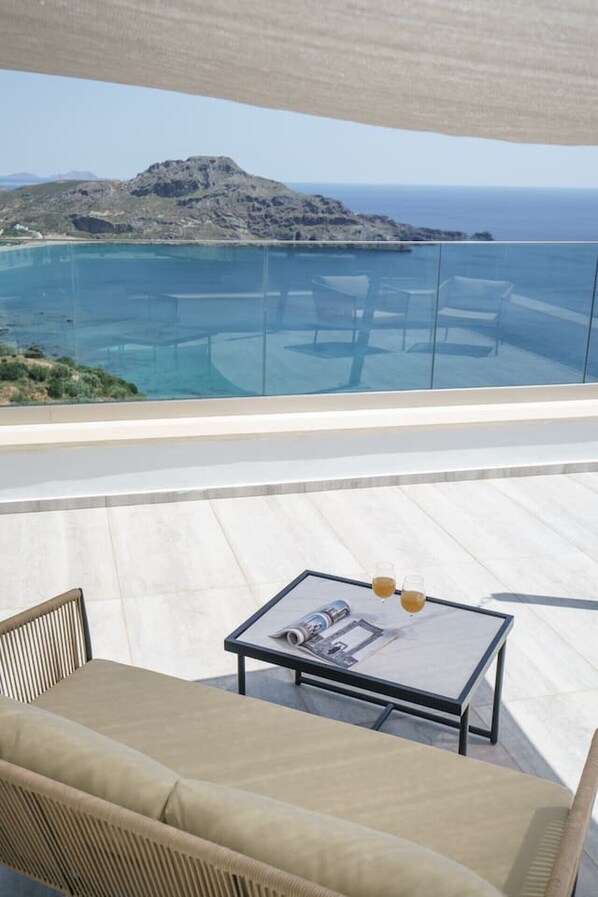 A balcony with a glass barrier, a sofa, a table with a magazine, and a glass of drink.