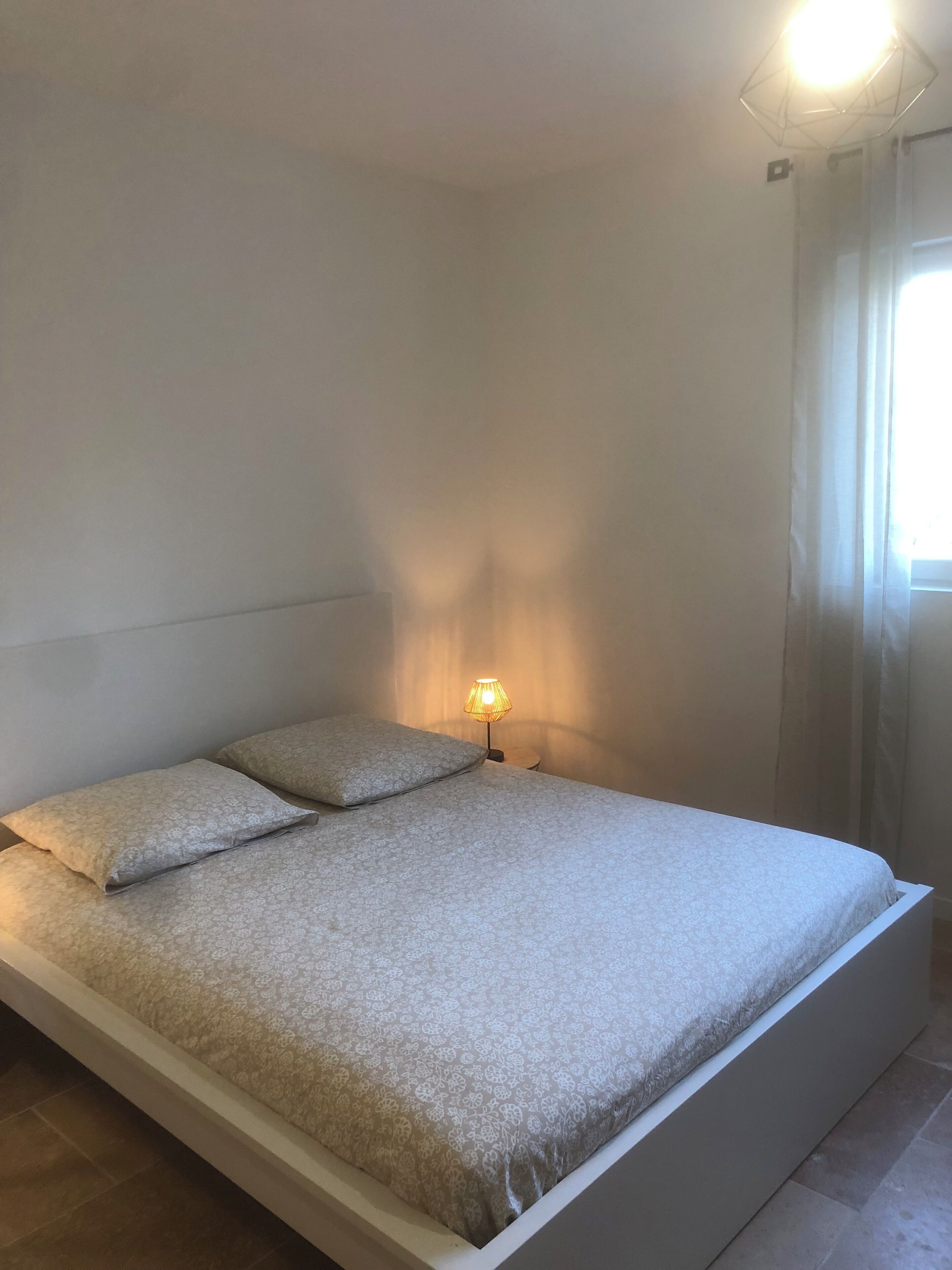 A bed with a patterned bedspread and two pillows, a bedside lamp, and a window with curtains.