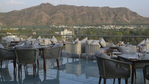 A rooftop terrace with wicker furniture and glass tables, overlooking a mountainous landscape. - Signature Hotel (Ajmer)