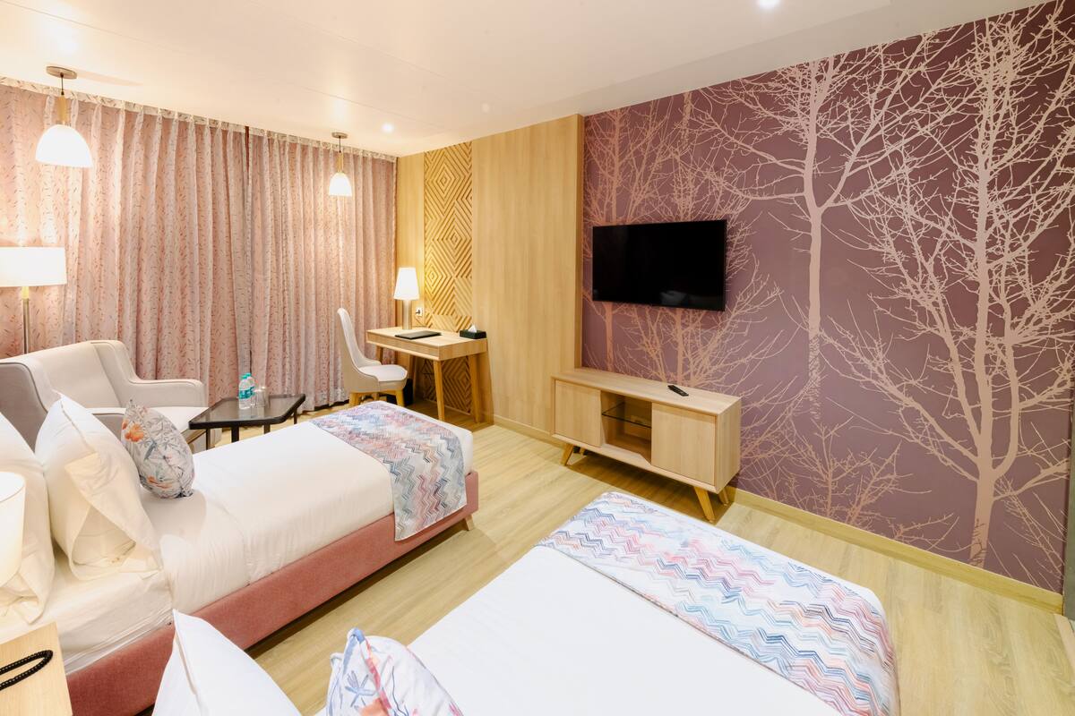 A hotel room with two beds, a desk, a chair, and a TV on the wall.