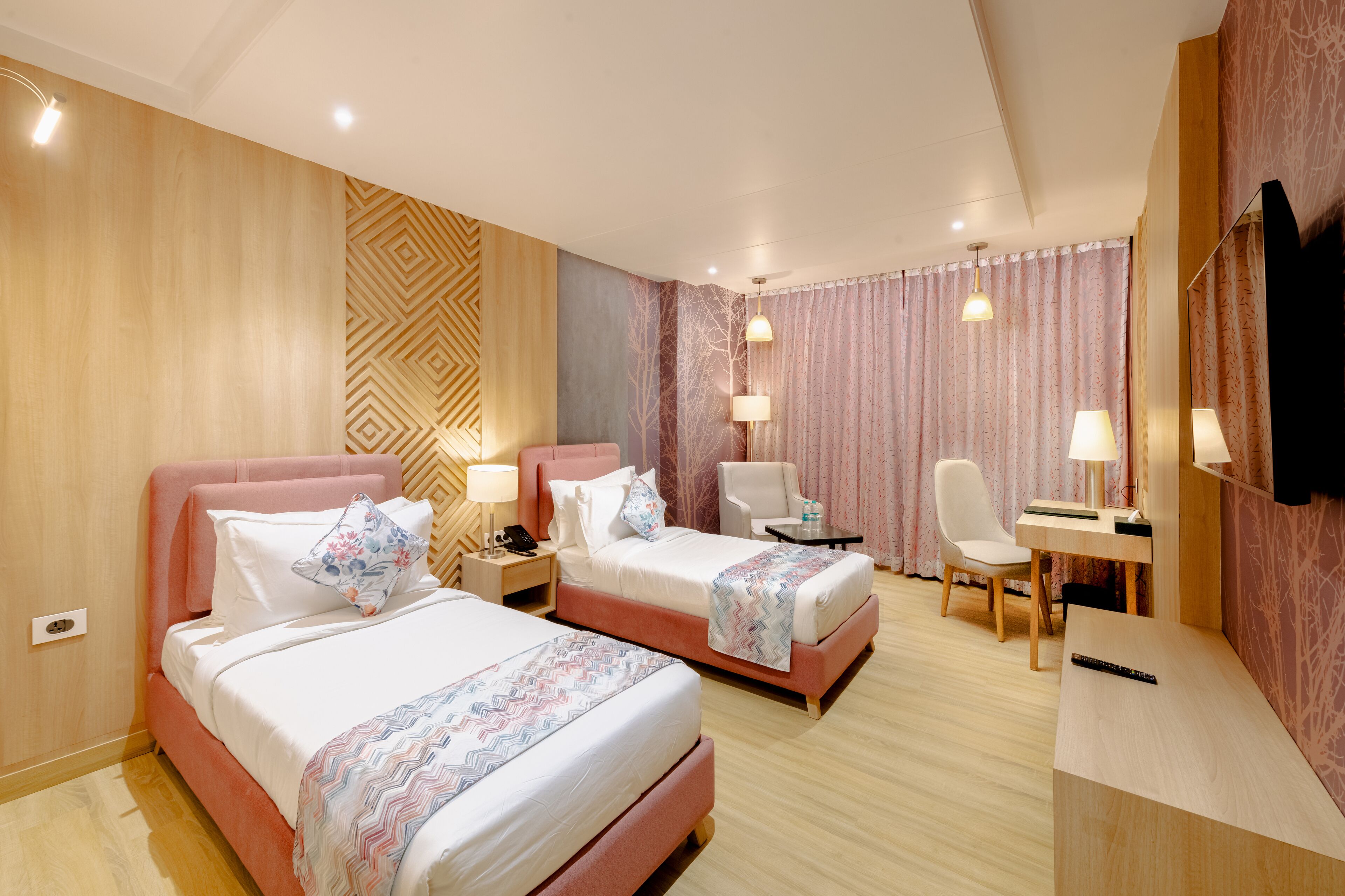 A hotel room with two beds, a desk, a chair, and a TV.