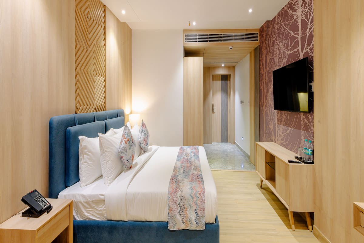 A modern bedroom with a large bed, a TV mounted on the wall, and a wooden floor.