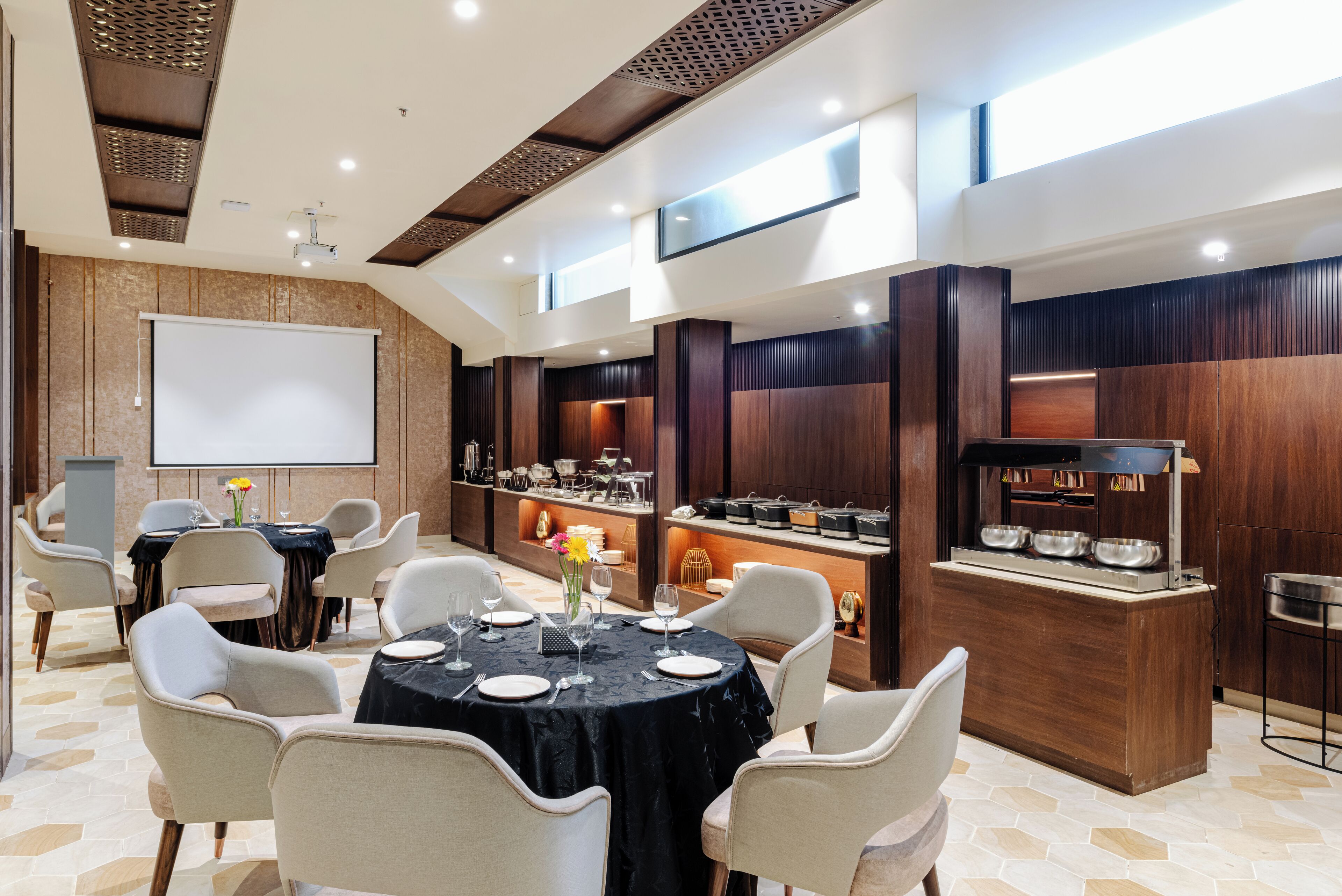 A conference room with a large white screen, round tables with chairs, and a buffet area with various dishes.
