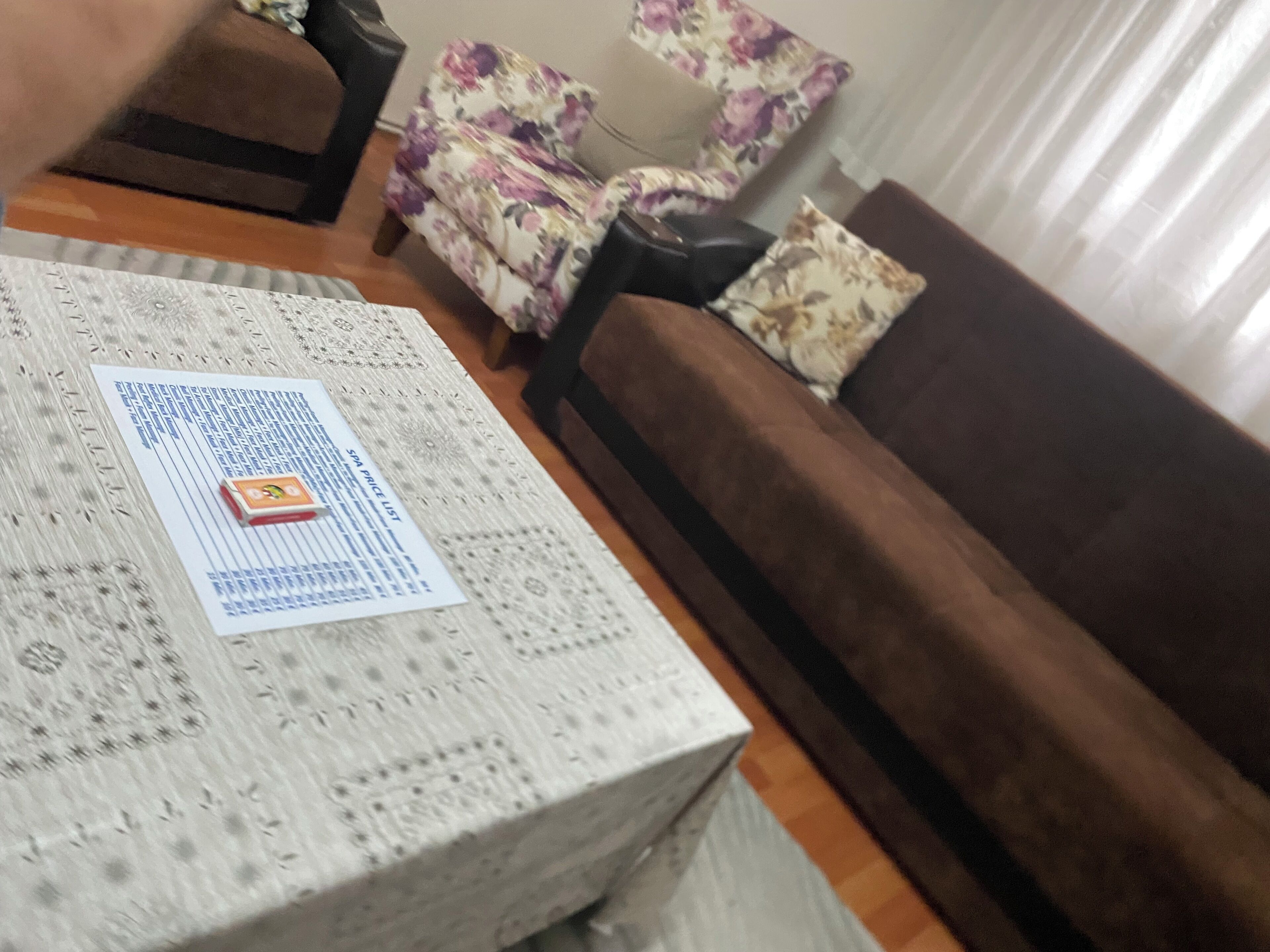 A living room with a patterned coffee table, a brown sofa, and a floral armchair.