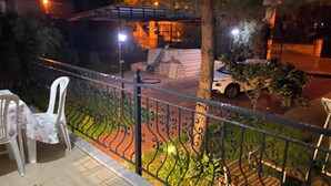 Un balcón con barandilla de metal, un coche blanco estacionado en la calle y un árbol.