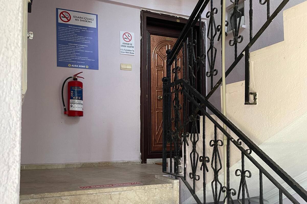 Uma escadaria com degraus de mármore e grades de ferro forjado, que leva a uma porta de madeira.
