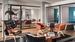 Spazio ufficio moderno con poltrone in pelle, un tavolo rotondo e una parete divisoria in vetro che separa l'area lavoro dalla sala da pranzo.