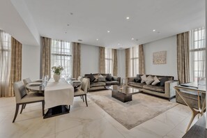 Un salon spacieux comprenant un coin repas, deux canapés, une table basse et une grande fenêtre avec des rideaux.